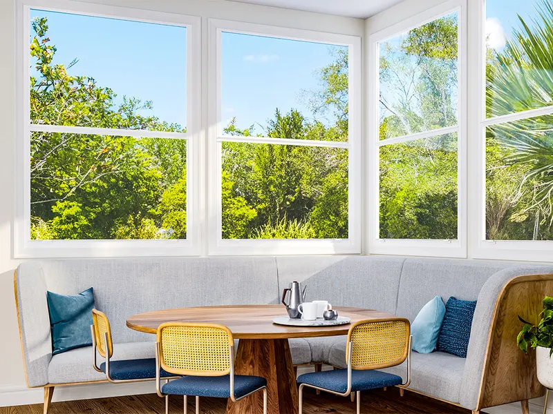 Breakfast nook with a corner of white single hung windows above a built-in bench and round table