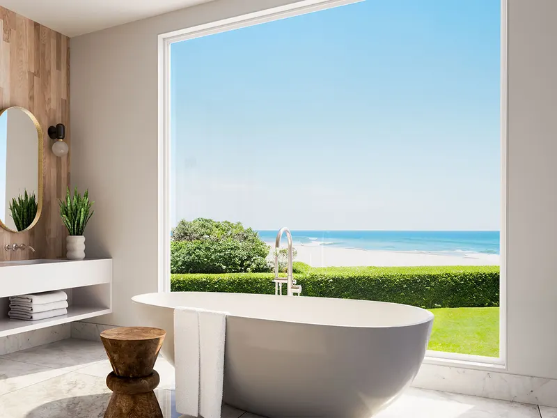 Bathroom with a freestanding tub in front of a large white picture window facing the ocean