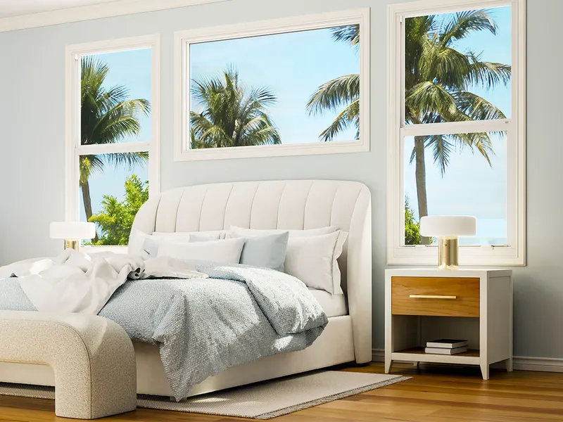 Bedroom with white single hung windows on either side of the bed and palms outside