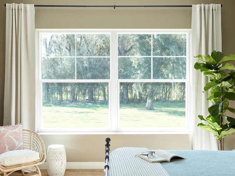 Bedroom with a pair of white single hung windows with grids framed by curtains