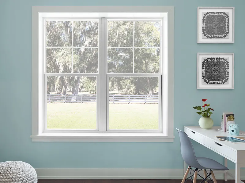 Pair of white single hung windows with grids in a light blue room with a desk