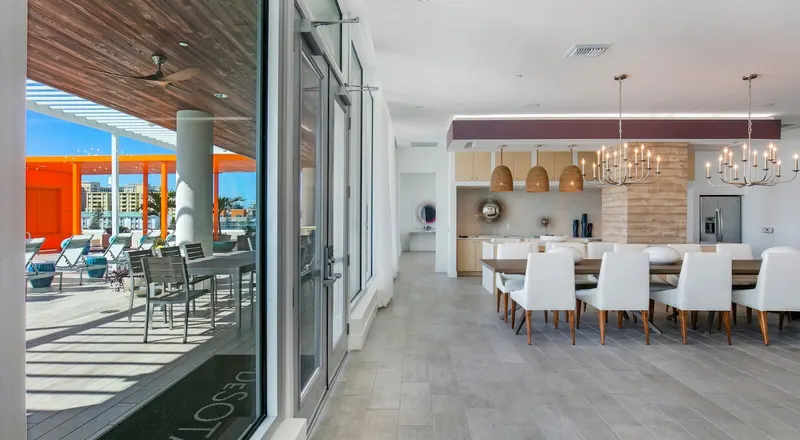 Clubhouse interior with a long dining table and pendant lights, with tall glass doors opening to a covered terrace