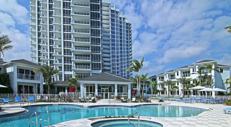 Resort pool and hot tub in front of low-rise buildings and a high-rise residential tower with many windows