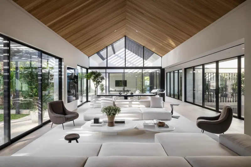 Bright great room with a vaulted wood ceiling, white sofas and floor-to-ceiling glass walls and doors on both sides