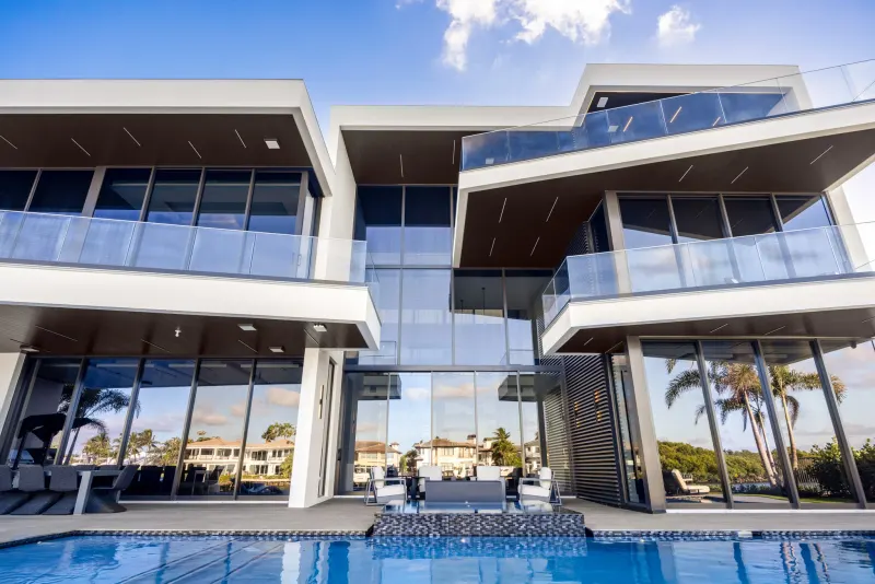 Modern two-story white house with large glass walls and balconies behind a swimming pool