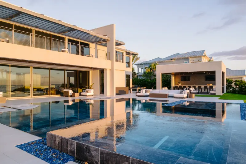 Modern house with full-height glass walls along a terrace, reflected in an infinity-edge swimming pool