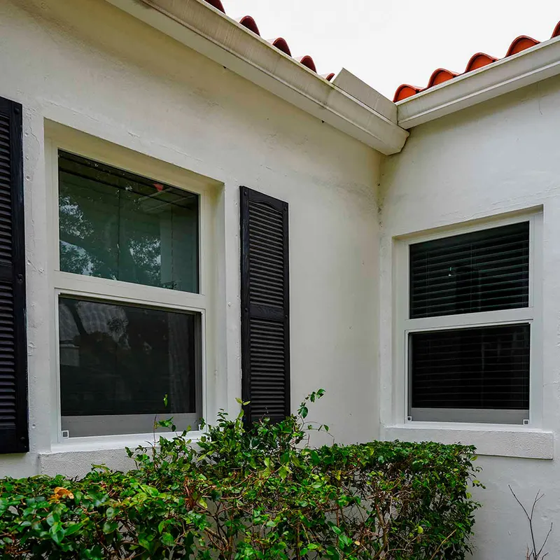 Exterior of a white stucco home with dark-framed windows beside black shutters