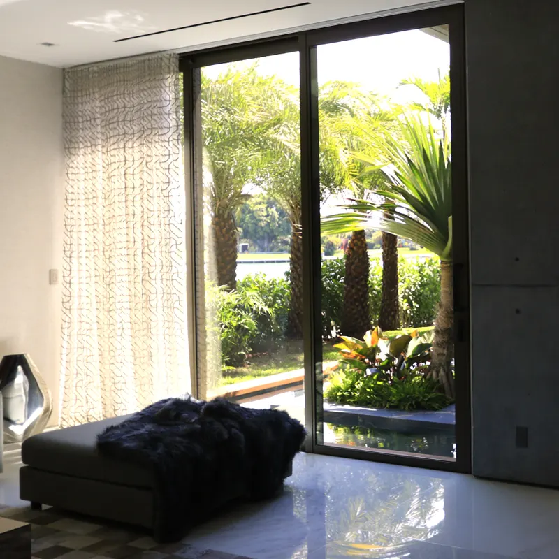 Bedroom with a polished floor and floor-to-ceiling dark-framed glass doors looking onto a tropical garden