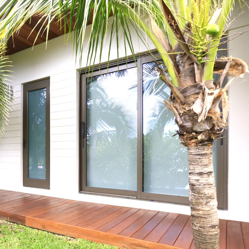 White house exterior with a dark-framed sliding glass door and window opening onto a wood deck, palm trunk in front