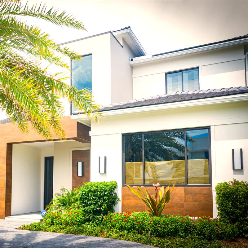 Modern two-story white house with large dark-framed windows and a wood-clad entry, landscaped front yard