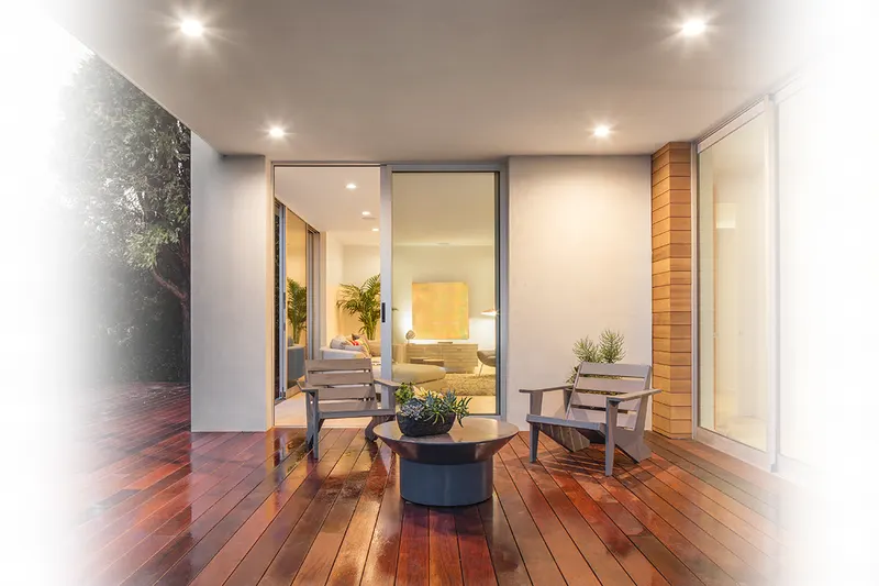 Living room with wood floors and lounge chairs beside large sliding glass doors opening to greenery