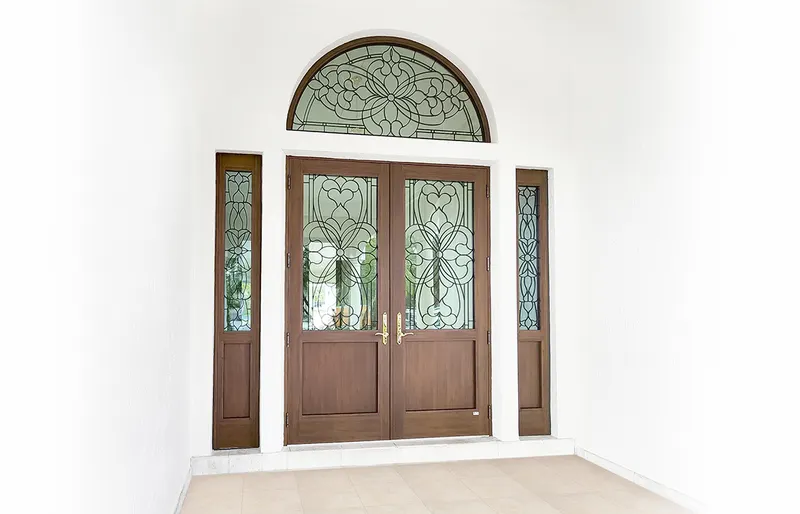 Wood-tone double doors with decorative glass, matching sidelites and an arched decorative glass transom