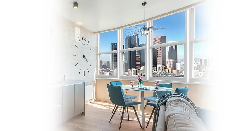 Dining area with tall windows overlooking a city skyline, round table and blue chairs