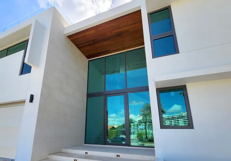 Modern white house entry with a tall dark-framed glass entrance under a wood-clad overhang, seen from below