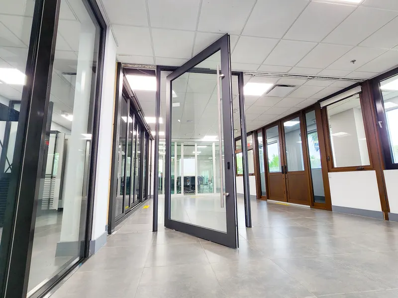 Dark-framed full-glass pivot door standing open in a showroom corridor