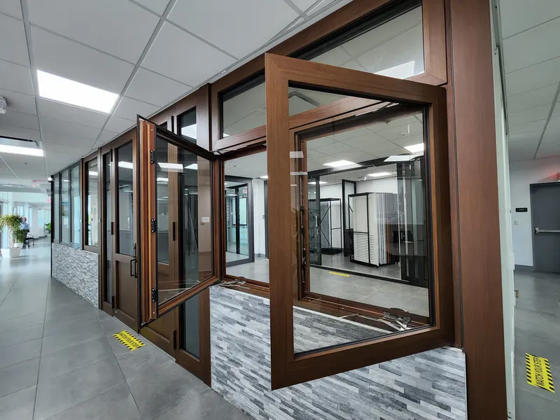 Wood-tone casement window sash swung open in a showroom display wall with a fixed transom above