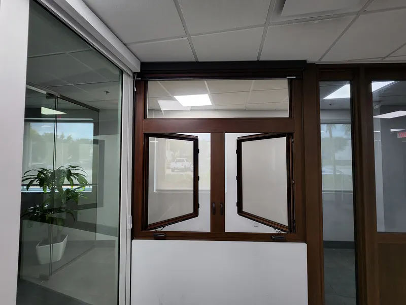 Pair of wood-tone casement windows partly open beneath a transom in a showroom wall