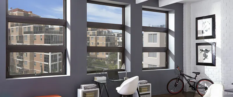 Row of dark-framed awning windows in a gray loft wall with a city view