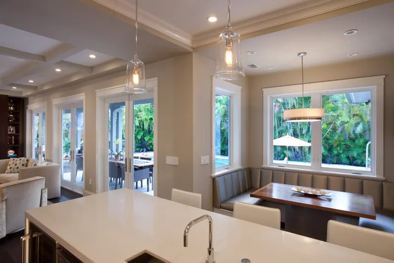 Open kitchen and dining area with large white-framed casement windows and French doors to a pool
