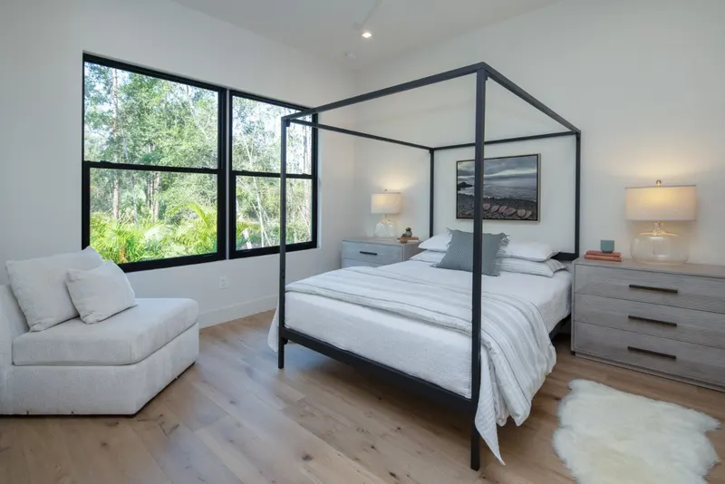 Bedroom with black-framed single hung windows beside a canopy bed and sitting chair