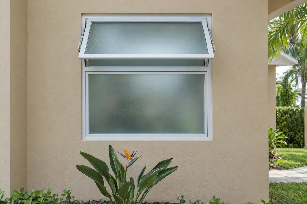 White awning window hinged at the top and opened outward above a fixed window, with privacy glass