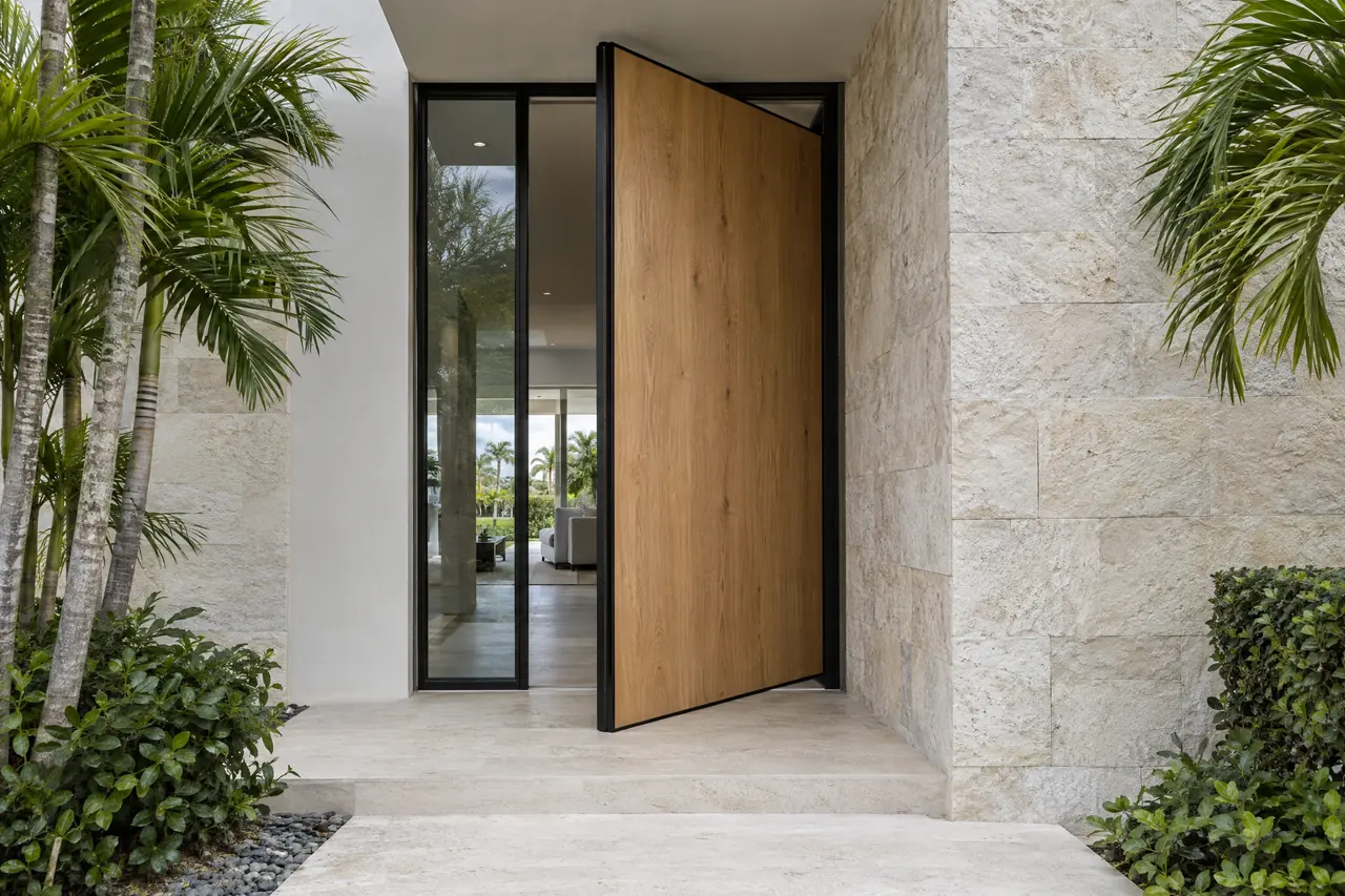 Oak pivot front door turned open on its offset pivot beside a glass sidelite and stone cladding