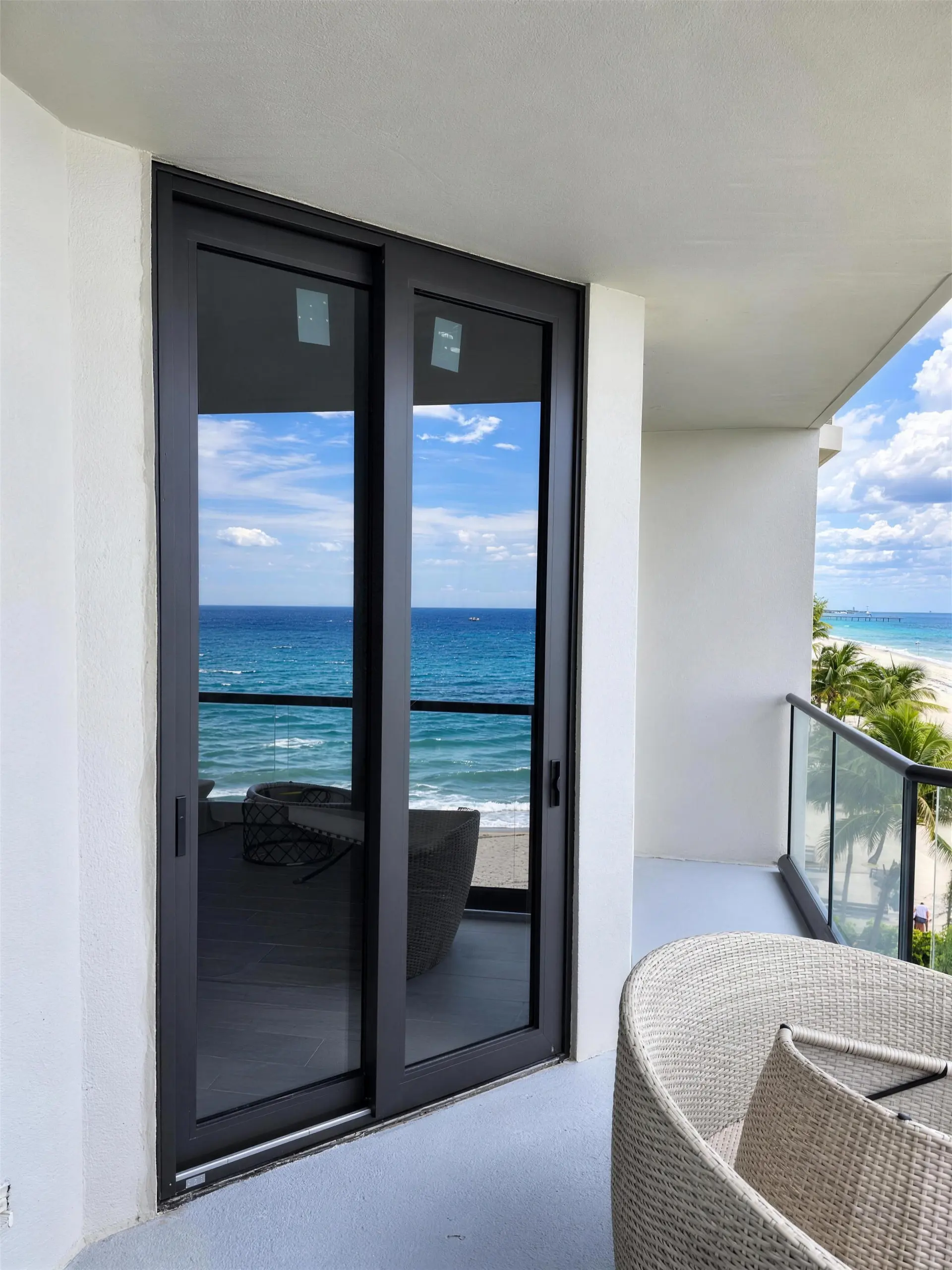 Dark-framed impact sliding glass door on an oceanfront condo balcony, with the Atlantic visible through the glass