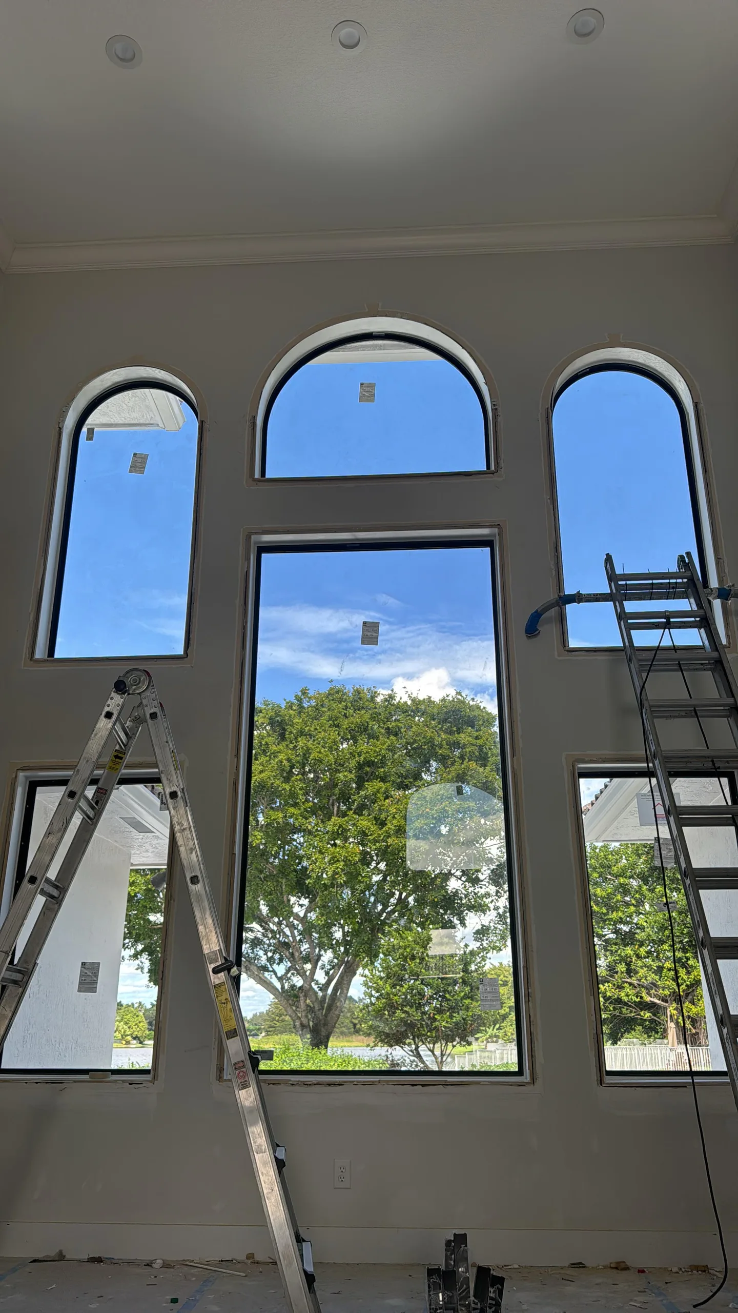 Arched and rectangular windows photographed during installation, with ladders and finish work visible.